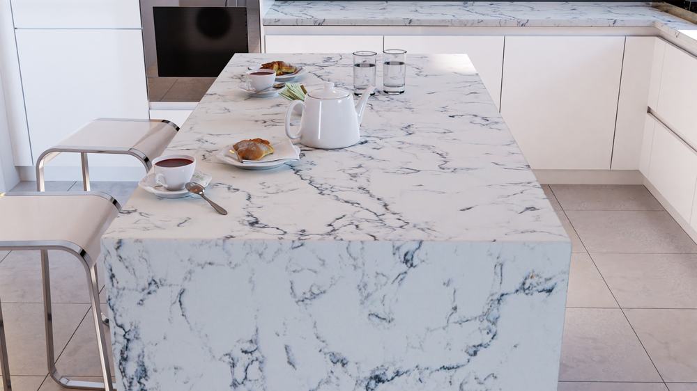 A modern kitchen with a white marble island countertop, two white chairs, a teapot, cups of tea, pastries, and glasses of water&mdash;showcasing the elegance achieved through expert stone restoration NYC. White cabinets and more marble surfaces complete the look.