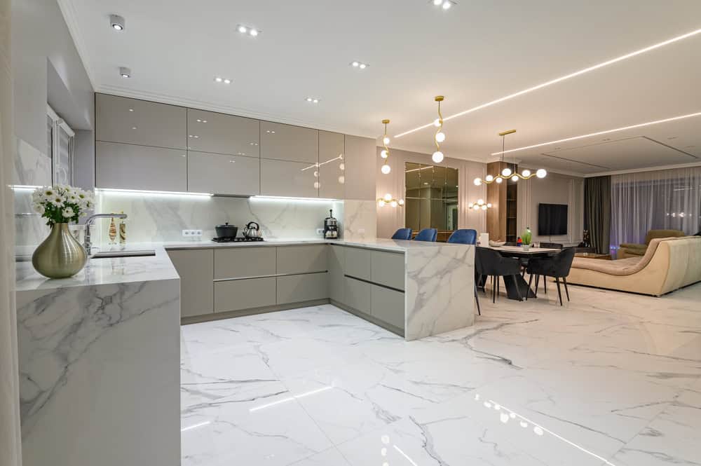 Modern open-plan kitchen and living area with marble floors and countertops, sleek beige cabinets, contemporary lighting, and elegant dining spaces—expert stone restoration NYC keeps every surface pristine.