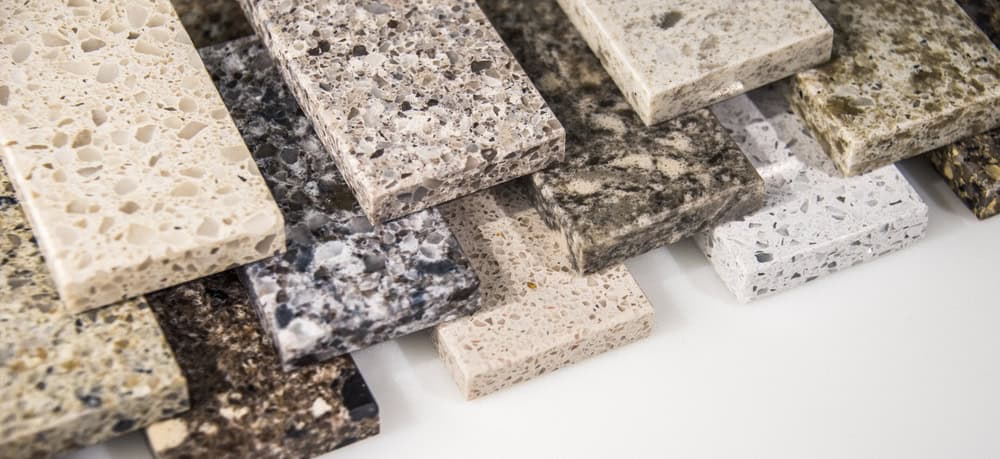 A variety of rectangular stone countertop samples with different colors and speckled patterns are arranged overlapping on a white surface, showcasing the quality materials often used in stone restoration NYC.