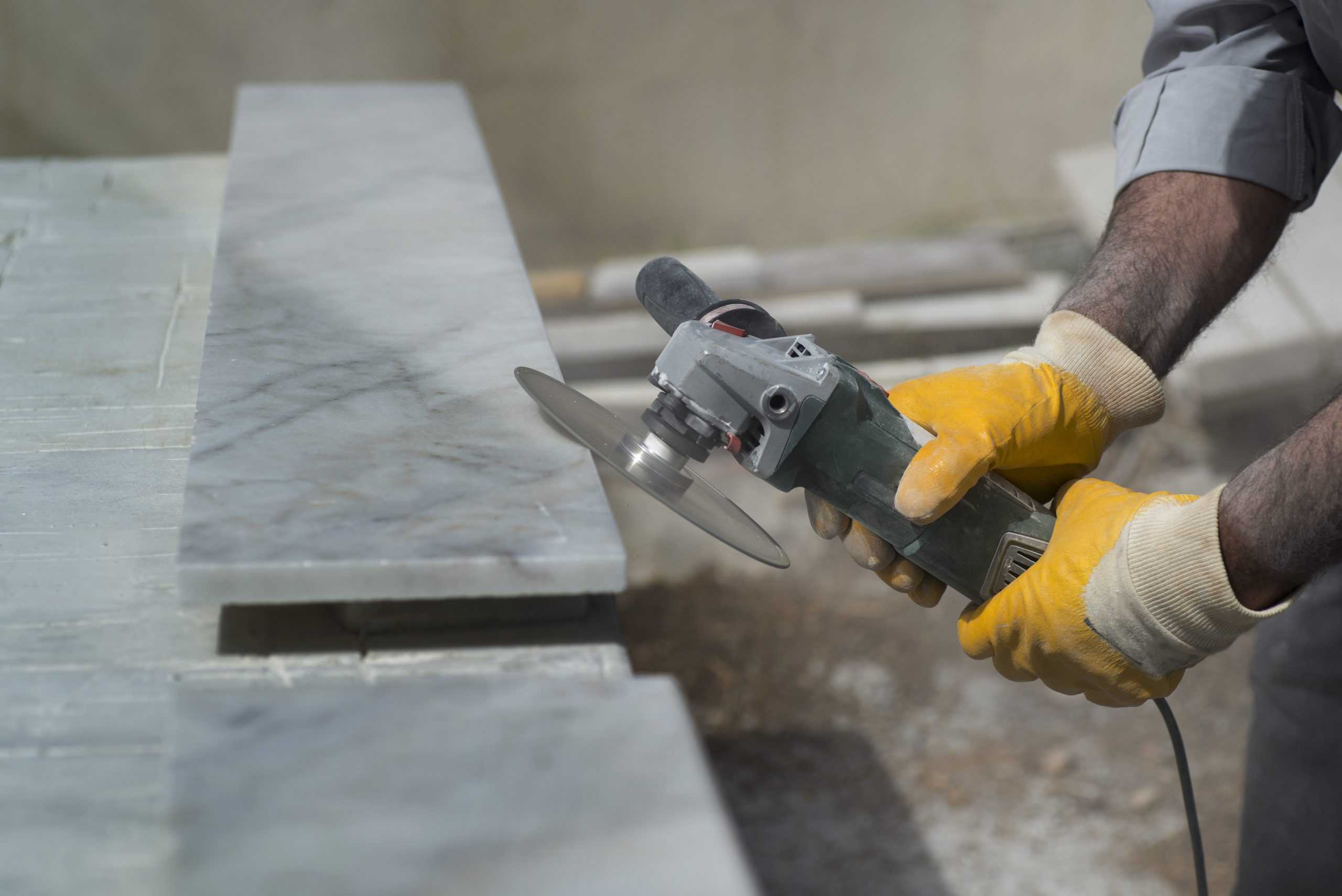 A person wearing yellow gloves uses an electric angle grinder to cut a slab of marble, showcasing the precision and skill often seen in stone repair NYC projects.